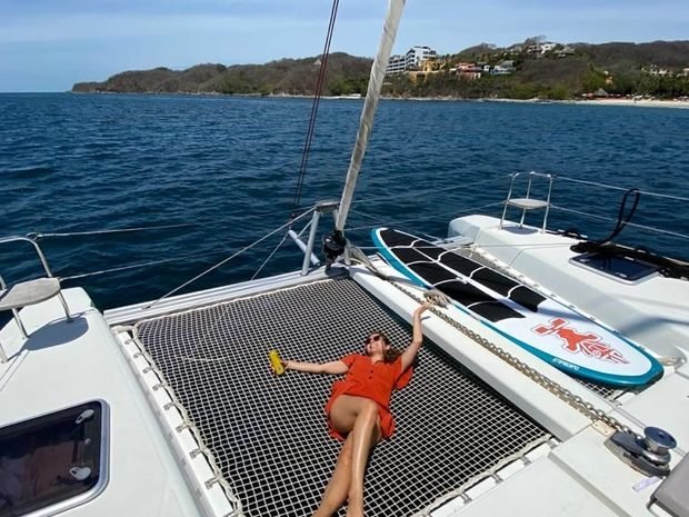 Someone lying on the bow netting with a drink, paddleboards stowed behind
